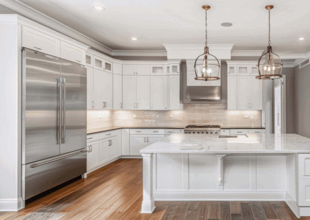 Modern white kitchen with stainless steel appliances, marble countertops, and pendant lighting, perfect for custom kitchen design and renovation by Aurea Kitchens.