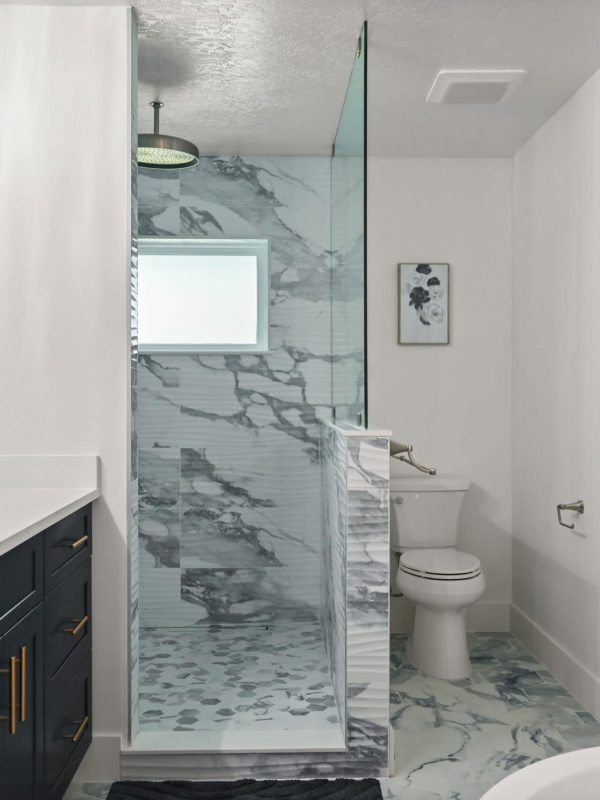 Modern luxury bathroom with marble accents, sleek navy vanity with gold hardware, glass walk-in shower, and minimalist design elements for a stylish and functional space.