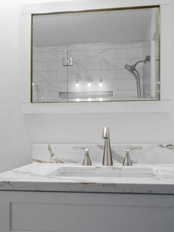 Modern bathroom vanity with marble countertop and sleek silver faucet, featuring a large mirror and white walls, exemplifying contemporary kitchen and bathroom design by Aurea Kitchens.