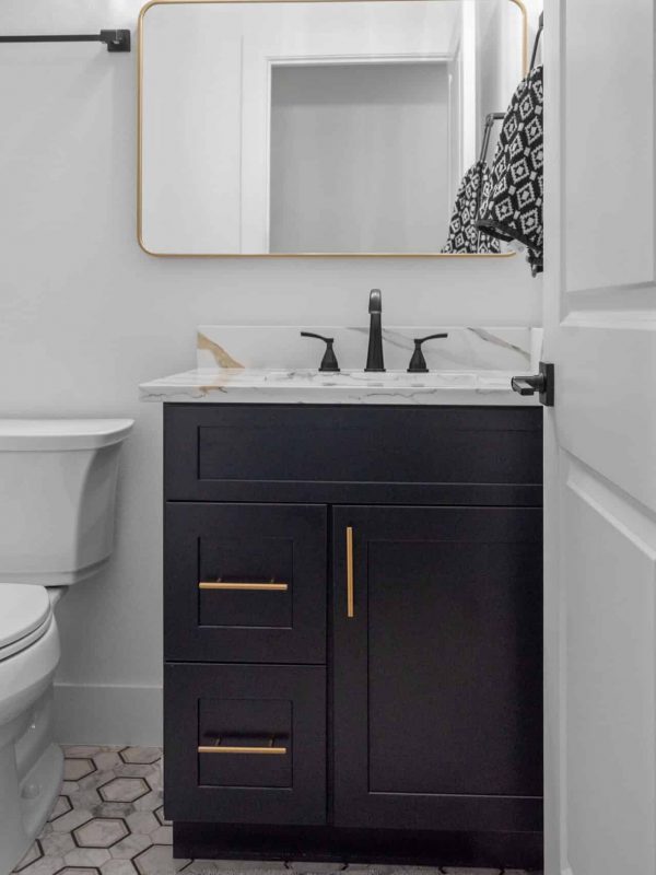 Modern bathroom with black vanity, marble countertop, and geometric tile flooring, showcasing expert design and build services by Aurea Kitchens. Suitable for stylish, functional spaces.