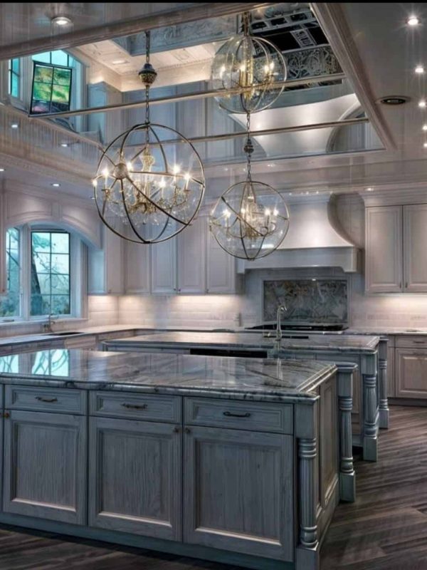 Luxurious kitchen with white cabinetry, marble island, elegant lighting fixtures, and large windows creating a bright, sophisticated space for cooking and entertaining.