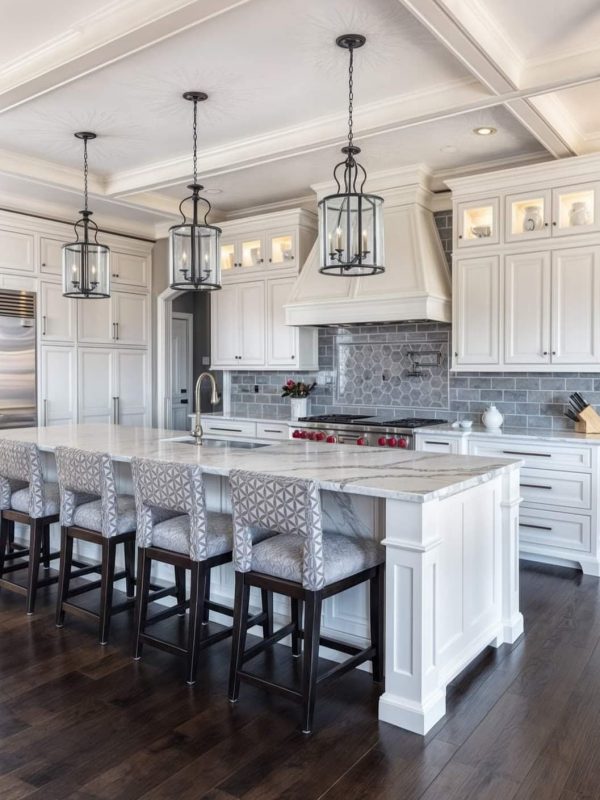 Luxurious white kitchen with marble island, pendant lighting, grey backsplash, and custom cabinetry, designed for modern luxury homes by Aurea Kitchens.
