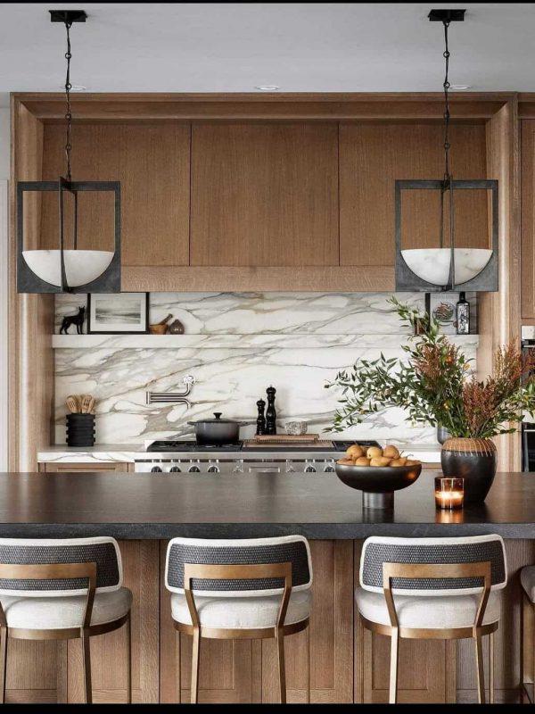 Sleek modern kitchen with wood and marble accents, stylish pendant lighting, and a large island with bar seating perfect for entertaining. Designed by Aurea Kitchens for contemporary home remodeling.