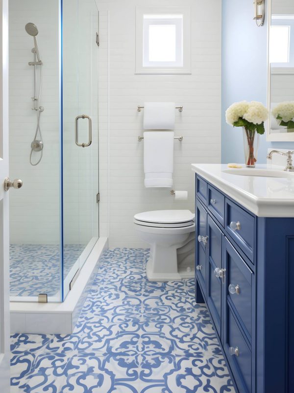 Bright white and blue bathroom with a walk-in shower, modern vanity with blue cabinetry, decorative patterned tile flooring, and minimalistic fixtures, showcasing expert design and craftsmanship.